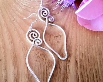 May include: A pair of silver-colored wire earrings featuring a teardrop-shaped frame with a double spiral design at the top. Each earring is suspended from a simple hook wire, showcasing a continuous metallic loop that forms an open, elongated shape.