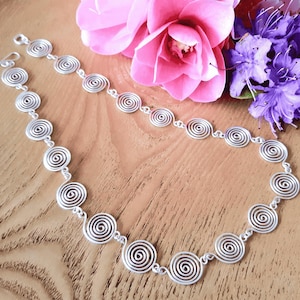 May include: A silver-toned necklace composed of a series of interconnected circular spiral links. The metal chain features a repeating pattern of identical wire-formed swirls, connected by small jump rings, ending with a simple hook-style clasp.