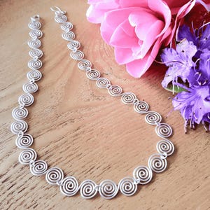Full view of a handmade silver Celtic Necklace with a hook clasp on a wooden surface with flowers