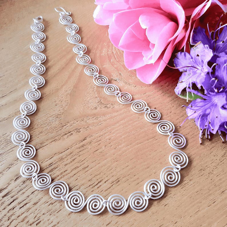 Full view of a handmade silver Celtic Necklace with a hook clasp on a wooden surface with flowers
