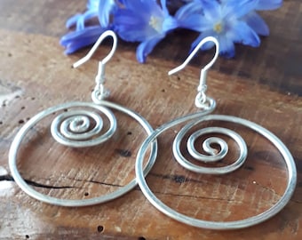 May include: A pair of silver-toned dangle earrings featuring a circular wire frame with an integrated spiral design in the center. The earrings are attached to standard silver-toned ear hooks for pierced ears, showcasing a metallic finish.