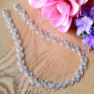 Full view of the handmade silver Celtic spiral necklace with a hook clasp on a wooden surface with flowers