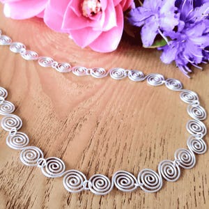 Detailed view of a silver spiral necklace on a wooden surface with flowers in the background