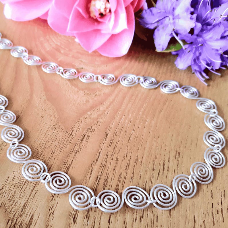 Detailed view of a silver spiral necklace on a wooden surface with flowers in the background