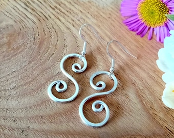 May include: Silver dangle earrings with a double swirl design. The earrings are made of wire and have a simple, elegant look.