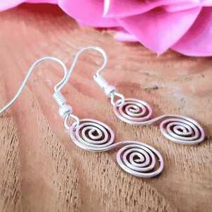 Side on view of a pair of Celtic Silver spiral handmade earrings on a wooden surface with a pink flower