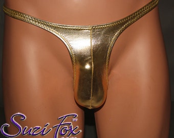 May include: A metallic gold thong featuring a shiny, reflective finish and visible zigzag stitching along the edges. The garment has a narrow waistband and a contoured front pouch. The text Suzi Fox .com is printed in purple and white in the corner.