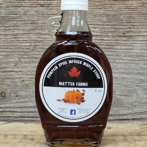 May include: A glass bottle of pumpkin spice infused maple syrup with a white label that says "Pumpkin Spice Infused Maple Syrup" and "Matter Farms". The label also features a small pumpkin and maple leaf graphic. The bottle is 8 ounces and has a white lid.