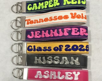 May include: Six colorful keychains with embroidered names and phrases, including "Camper Keys", "Tennessee Vols", "Jennifer", "Class of 2023", "Hussan", and "Ashley".