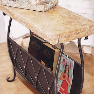 May include: A decorative side table with a stone top and a dark metal magazine rack. The table holds books and a magazine with a woman in a red top. The table is on a wood floor.