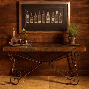 May include: A rustic console table with a copper-toned top and ornate metal legs. A framed print of liquor bottles hangs above the table. Decorative bottles and a small plant in a pot are displayed on the table's surface.