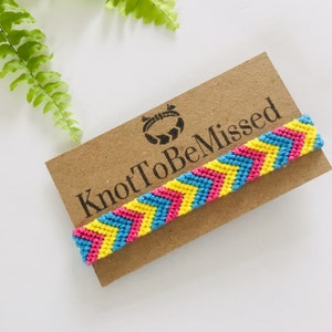 May include: A chevron friendship bracelet in pink, blue, and yellow, displayed on a brown card. The card reads "KnotToBeMissed". This handmade bracelet is a vibrant accessory. The bracelet is a handmade accessory.