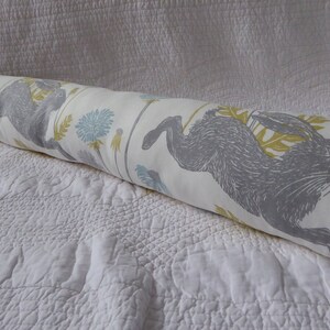 May include: A white bolster cushion with a grey and yellow print of running hares and dandelions.