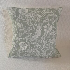 May include: A square throw cushion featuring a sage green background with a repeating white botanical pattern of flowers, leaves, and vines. The fabric has a smooth texture and the design covers the entire front surface of the cushion.