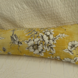 May include: A long, yellow bolster pillow with a floral and bird print. The pillow has a white background with black and grey floral and bird designs.