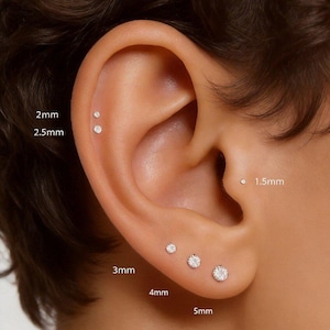 Peut inclure: Gros plan sur une oreille ornée de plusieurs petits clous d'oreilles ronds en diamant. Les tailles varient de 1,5 mm à 5 mm. Les boucles d'oreilles sont portées, mettant en valeur leurs différentes tailles.