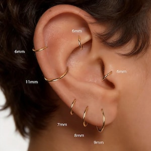 Op de afbeelding: Close-up van een oor versierd met meerdere gouden oorringen. De oorbellen variëren in grootte, met afmetingen van 6 mm, 7 mm, 8 mm, 9 mm en 11 mm. De oorringen zijn eenvoudig en elegant en tonen een minimalistische sieradenstijl.