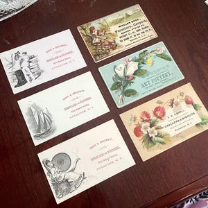 May include: A collection of vintage advertising cards, featuring illustrations and text. The cards showcase various businesses, including furniture, art pottery, and crackers. The color palette includes soft pastels and sepia tones, with detailed drawings and lettering.
