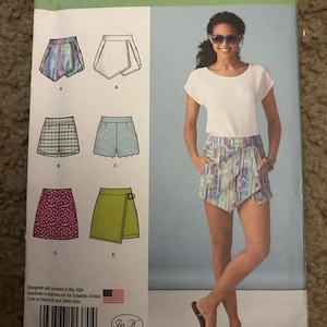 Op de afbeelding: Simplicity naaipatroon 1370 D5 voor shorts en rokken in maten 30-38. De envelop bevat illustraties van vijf kledingvariaties, waaronder wikkelshorts, shorts met patronen en rokken, naast een foto van de afgewerkte wikkelshorts.