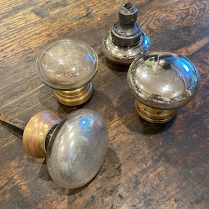 May include: Four antique door knobs. Two have clear glass globes with gold-coloured bases. One has a silver-coloured globe with a gold-coloured base. The fourth knob is silver with a brass base and a metal rod.