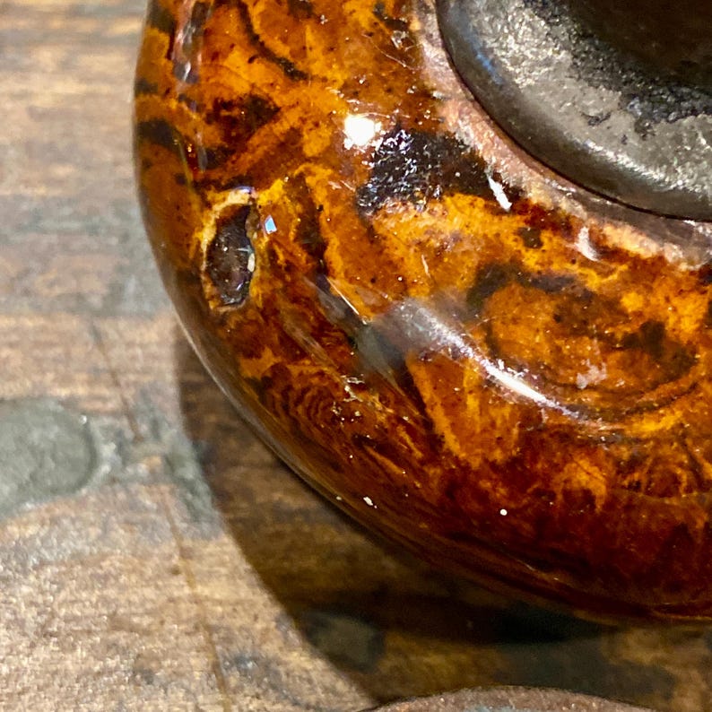 May include: A round, polished door knob featuring a glossy, marbled finish with swirling patterns of dark brown, amber, and golden yellow hues. The surface has a reflective, smooth texture with a dark metallic base visible at the top edge.