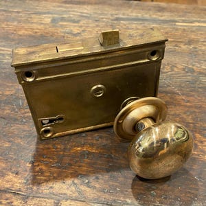 Puede incluir: Juego de cerradura de puerta de latón antiguo con una cerradura de embutir rectangular y un pomo redondo. La cerradura tiene una cerradura y un pestillo. El pomo es ovalado y tiene una placa trasera circular. El juego es de latón.