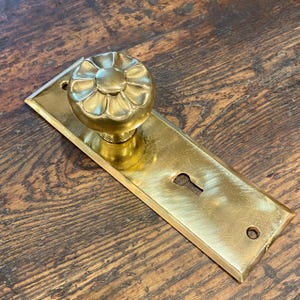 May include: A vintage brass door knob and plate set. The knob has a floral design, and the rectangular plate features a keyhole and mounting holes. The hardware has a warm, golden hue and shows signs of age.