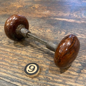 May include: Antique door knob with a dark brown, oval-shaped wooden handle and a metal rod. The knob has a glossy finish and a visible wood grain pattern. A small wooden disc with the number 9 is also present.