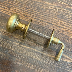May include: A vintage brass door knob set with a round knob, two circular backplates, and a lever handle. The set includes a threaded rod for installation. The brass has a warm, aged patina.