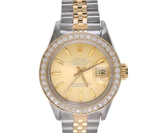 May include: A gold and silver Rolex Datejust watch with a diamond bezel and a champagne-colored dial. The watch has a two-tone bracelet and a date window at the 3 o'clock position.