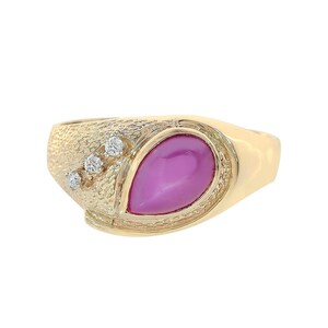 Op de afbeelding: Een gouden ring met een getextureerde band en een grote roze edelsteen in het midden. Drie kleinere diamanten zijn op de band gezet.