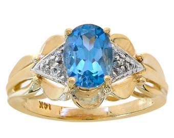 Op de afbeelding: Een gouden ring met een blauwe topaas edelsteen en twee kleinere diamanten. De ring heeft een bloemmotief en is gemarkeerd met "14K".