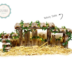 Può includere: Un presepe in legno con tetto di paglia, una recinzione e una scala. Il presepe è decorato con verde e luci. Il testo "Nativity Stable" è scritto sull'immagine.