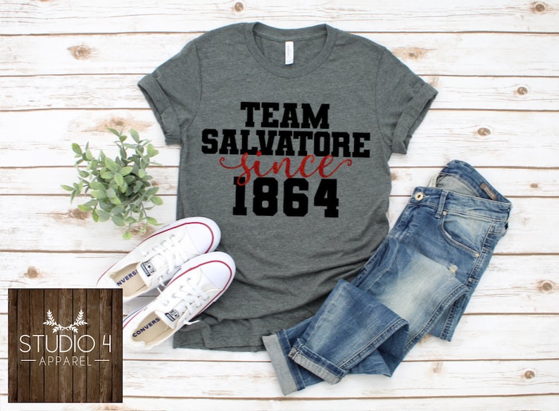 May include: Gray t-shirt with black text that reads "Team Salvatore since 1864". The text "since" is in red cursive.
