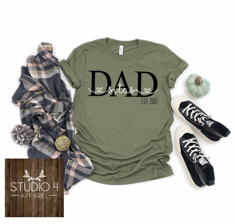 May include: Green t-shirt with black text that reads "DAD Silas EST. 2021" with two small hearts on either side of the name.
