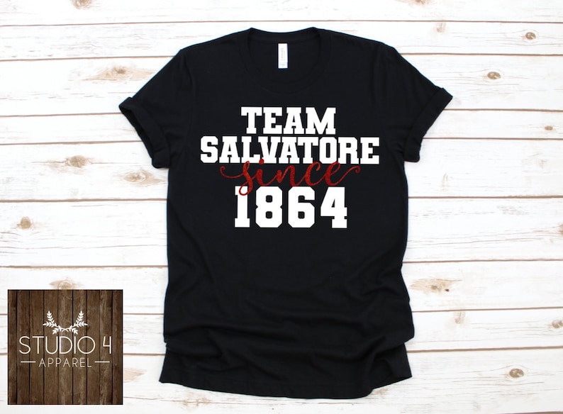 May include: Black t-shirt with white text that reads "Team Salvatore since 1864". The word "since" is written in cursive and the year 1864 is in red.
