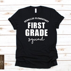 May include: Black t-shirt with white text that reads "DeValles Elementary First Grade Squad".