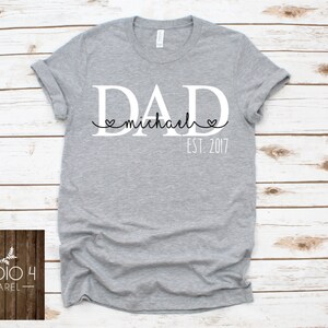 May include: Gray t-shirt with white text that reads "DAD michael EST: 2017" with two small hearts around the name.