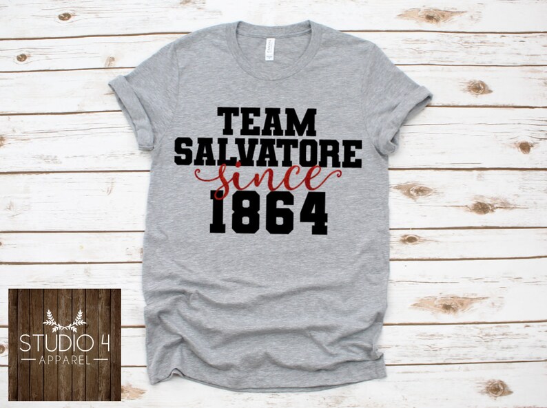 May include: Gray t-shirt with black text that reads "Team Salvatore since 1864". The word "since" is in red cursive.