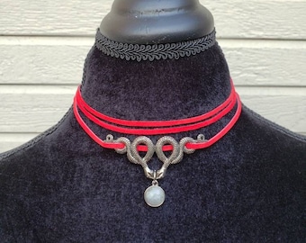 May include: A red choker necklace with a silver snake pendant and a round, light blue stone. The necklace is layered with two strands of red cord.
