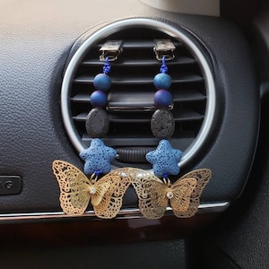 May include: Two car air freshener charms with blue and purple beads, lava rock, and blue star charms. The charms are attached to gold butterfly shaped clips.