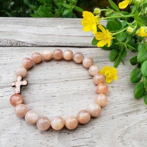 May include: A sunstone bracelet with a copper cross charm. The bracelet is made of natural sunstone beads and is a beautiful and unique piece of jewelry.