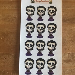 May include: A sheet of stickers featuring a Day of the Dead-themed design. Each sticker depicts a stylized skull with black hair, a purple dress, and a decorative collar. The sheet has the text "Danny's Planner Cuties".