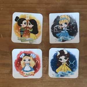 Puede incluir: Cuatro pegatinas cuadradas con princesas de Disney como signos del zodíaco. Las pegatinas son blancas con un fondo de acuarela y una cinta azul con el nombre del signo del zodíaco. Los signos del zodíaco son Géminis, Cáncer, Aries y Tauro. Las princesas son Mulan, Cenicienta, Alicia y Bella.