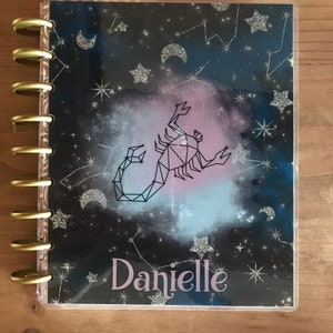 May include: A black and blue planner cover with a silver glitter design. The cover features a constellation of stars and a scorpion. The text "TODAY" is at the top of the cover and the name "Danielle" is at the bottom.