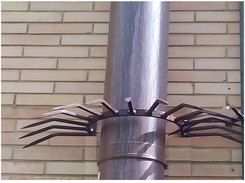 May include: A metal chimney cap with multiple pointed prongs to prevent birds from nesting. The cap is attached to a round, gray chimney pipe.