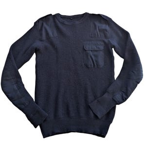 May include: Navy blue sweater with reinforced patches on the shoulders, elbows, and a chest pocket. The sweater has a ribbed texture and a crew neck. A classic, durable garment.