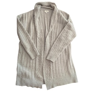 May include: A light beige open-front cardigan sweater. The sweater has a shawl collar and long sleeves. The knit fabric has a textured pattern on the sleeves and a ribbed pattern on the body. The sweater is a neutral color and appears to be made of a soft material.