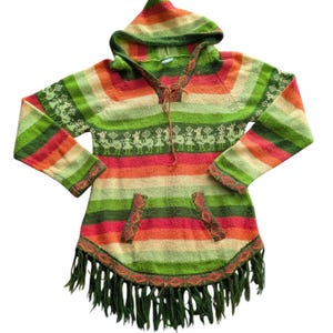 May include: A colorful, hooded poncho with horizontal stripes in shades of green, orange, and red. The poncho features a fringe hem, a kangaroo pocket, and a decorative pattern of llamas. The hood is also striped.