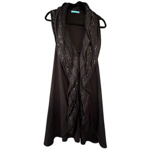 May include: A sleeveless black vest with a decorative, ruffled collar. The collar features a textured, embellished design. The vest is hanging on a black hanger against a white background.